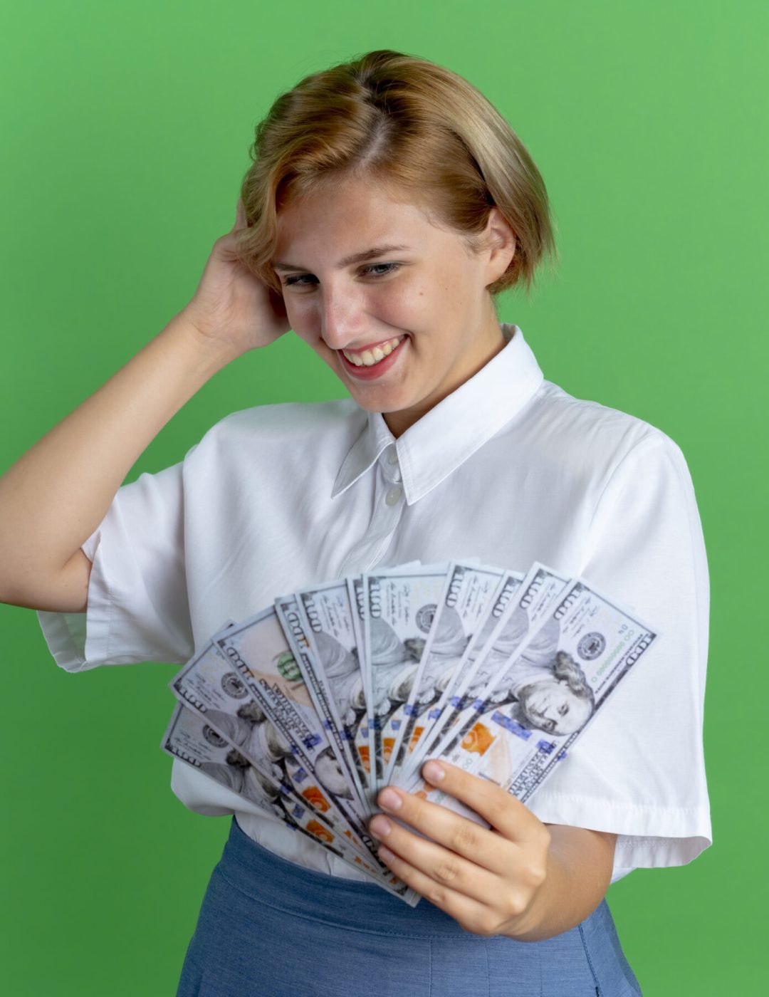 young smiling blonde russian girl holds and looks at money puts hand on head isolated on green background with copy space