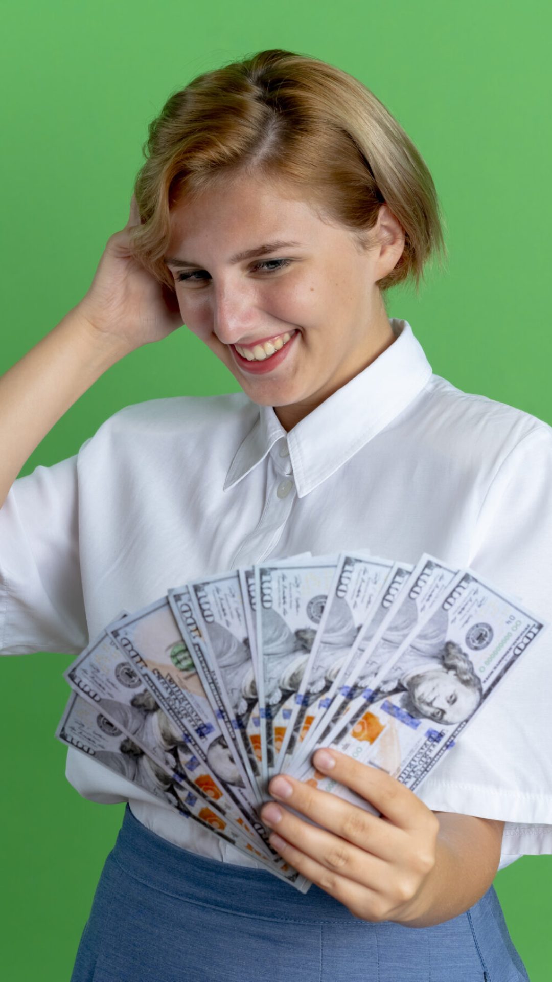 young smiling blonde russian girl holds and looks at money puts hand on head isolated on green background with copy space